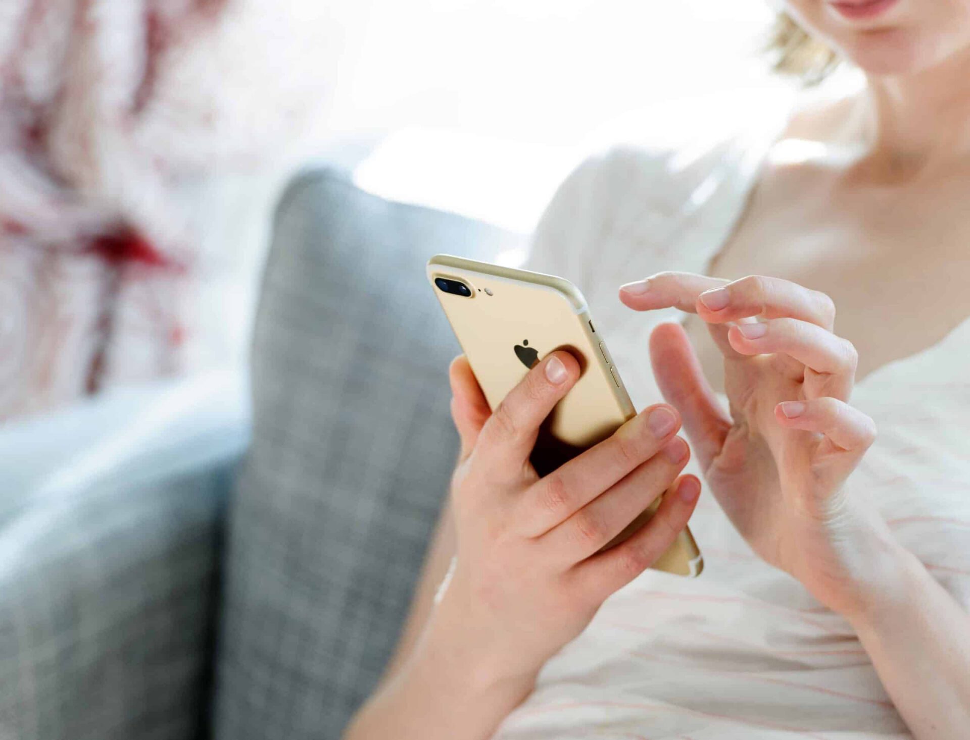 A woman sitting on a couch, using an iPhone, focusing intently on the screen as she explores web tracking services with one hand. Only her hands and the phone are in clear view.
