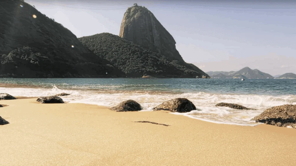 A serene beach view with sugarloaf mountain in the background, featuring golden sands, scattered rocks, and gentle waves under a clear sky. What's Your Seashore?