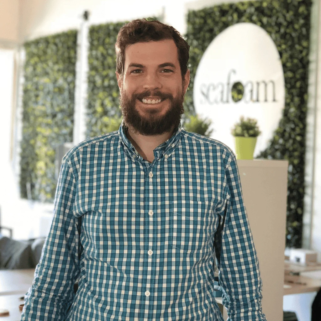 A smiling man with a beard wearing a blue and green checked shirt, standing in an office with a green plant wall and the "digital marketing" logo "seaform" in the background.