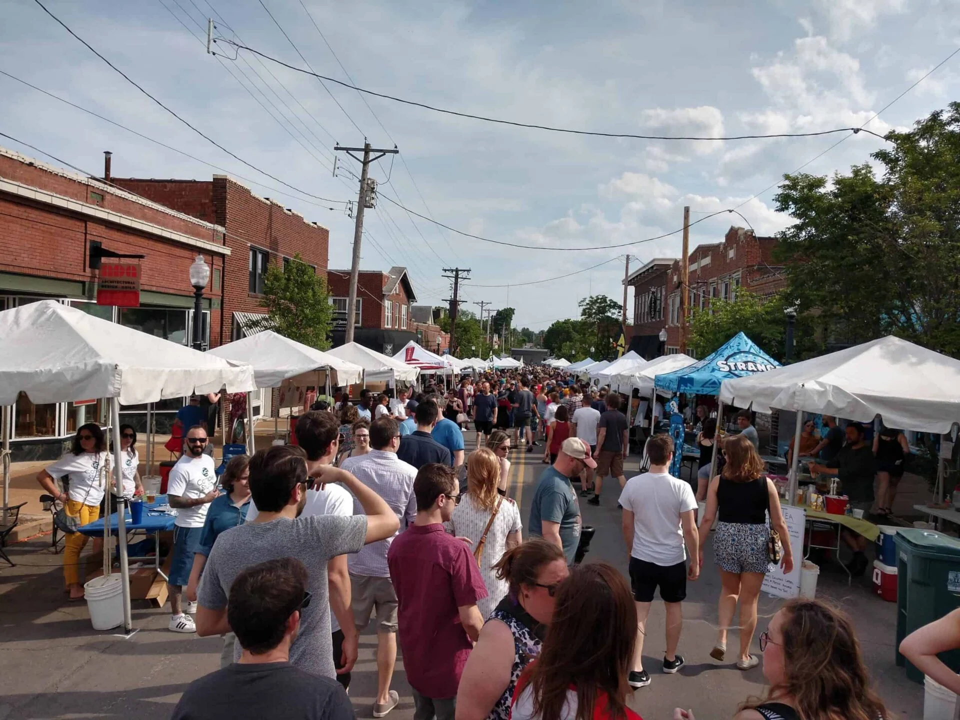 A bustling Taste of Maplewood festival with numerous people and vendor tents lining both sides of the street under a clear sky.