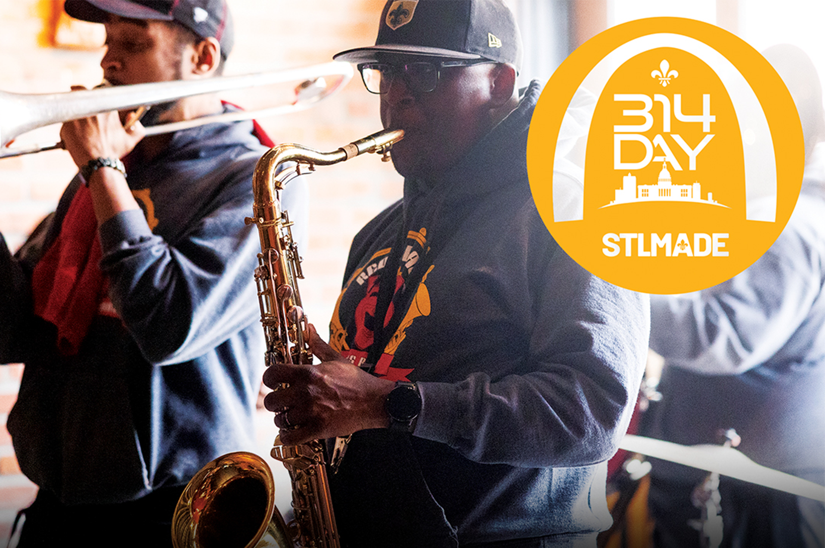 Two musicians, dressed casually in caps, play a trombone and saxophone against a brick wall. The "314 Day STLMade" logo highlights the scene, perfectly capturing St. Louis marketing flair in the upper right corner.