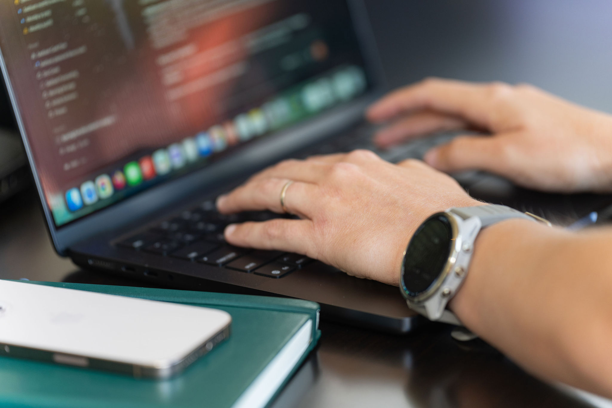 Hands typing a reply on a laptop keyboard, with a smartwatch on one wrist and a phone on the desk